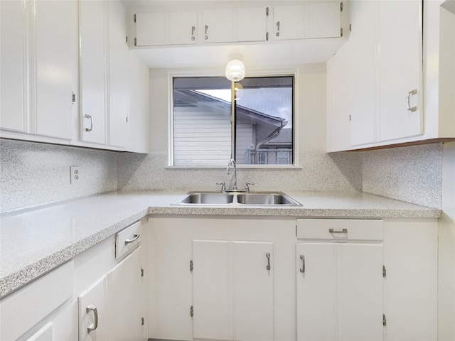 kitchen featuring light countertops, backsplash, a sink, and white cabinetry