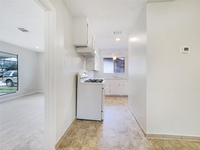 kitchen featuring visible vents, white gas range oven, and white cabinetry