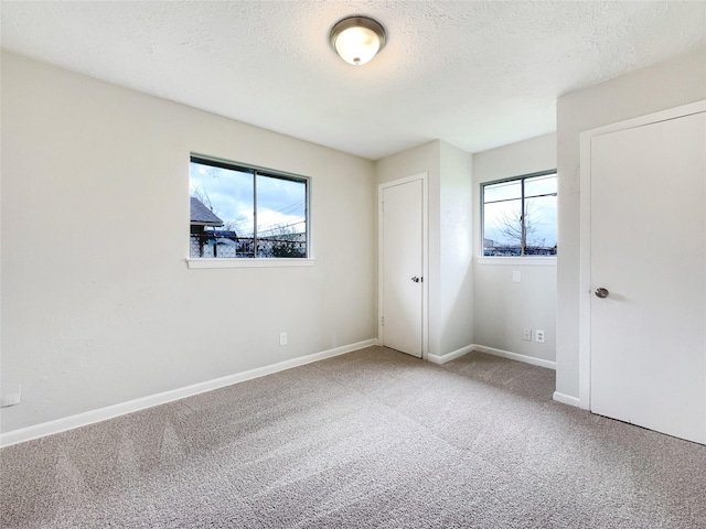 unfurnished bedroom with a textured ceiling, multiple windows, and carpet