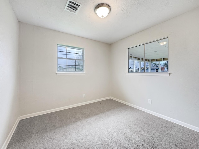 carpeted spare room featuring visible vents, a textured ceiling, and baseboards