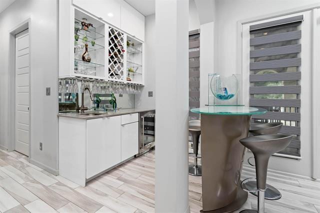 bar with sink, beverage cooler, white cabinets, and light wood-type flooring