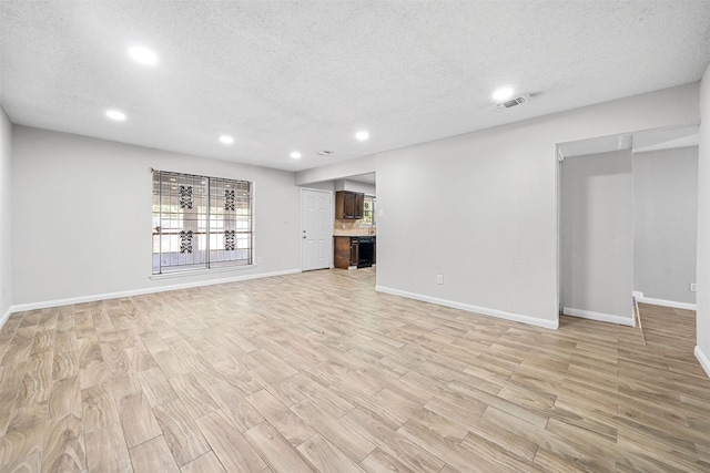 basement featuring light wood-type flooring, visible vents, a textured ceiling, and baseboards