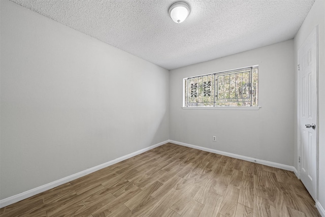 empty room with light wood-type flooring, baseboards, and a textured ceiling