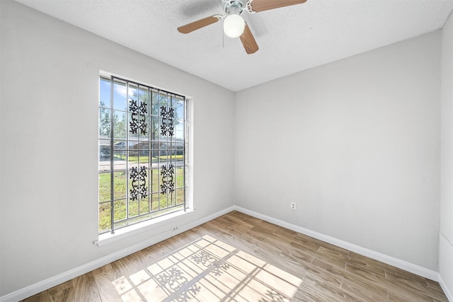 spare room with a textured ceiling, ceiling fan, light wood finished floors, and baseboards