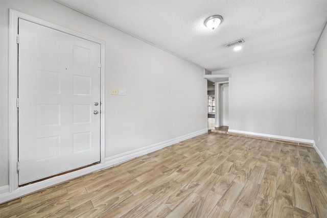 empty room featuring light wood finished floors, baseboards, visible vents, and a textured ceiling