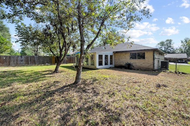 back of house with brick siding, a fenced backyard, central AC, and a yard