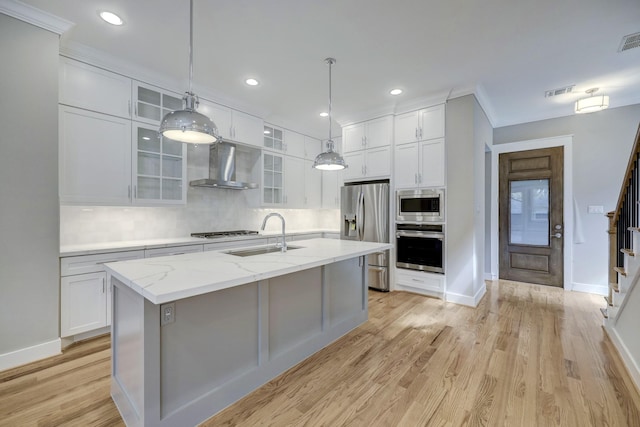 kitchen with appliances with stainless steel finishes, sink, white cabinets, a center island with sink, and wall chimney exhaust hood