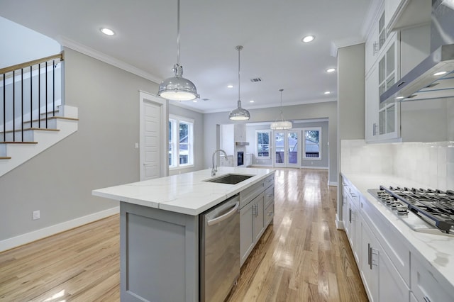 kitchen with sink, appliances with stainless steel finishes, white cabinetry, an island with sink, and wall chimney exhaust hood