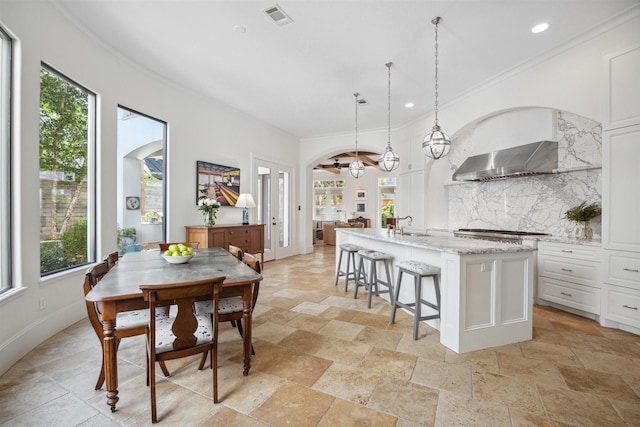 kitchen featuring white cabinetry, backsplash, hanging light fixtures, a kitchen island with sink, and light stone countertops