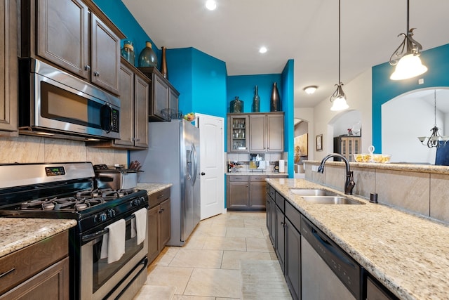 kitchen featuring sink, stainless steel appliances, dark brown cabinetry, decorative backsplash, and decorative light fixtures