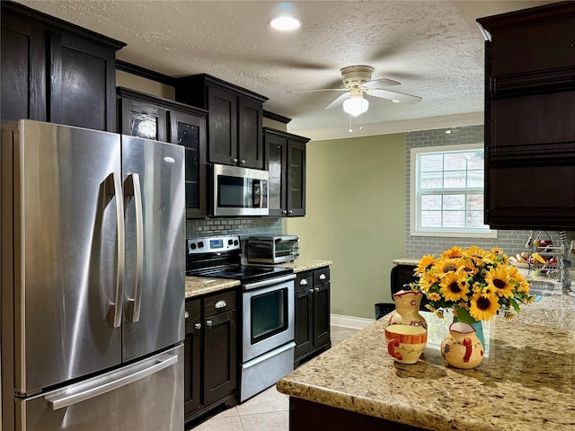 kitchen featuring ceiling fan, appliances with stainless steel finishes, backsplash, light stone counters, and light tile patterned flooring