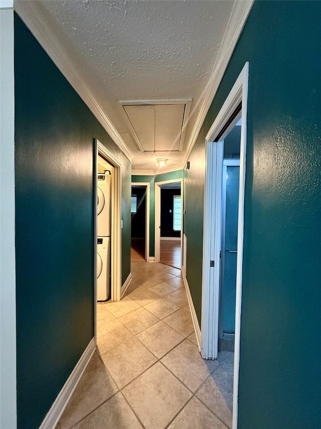 corridor featuring stacked washer and dryer, ornamental molding, a textured ceiling, and light tile patterned floors