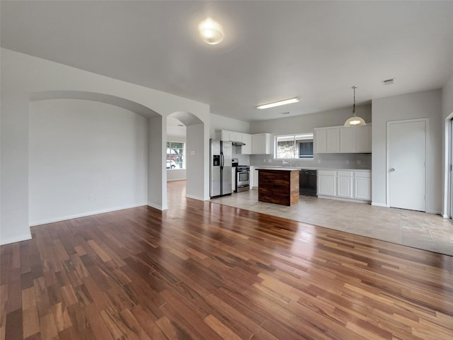 unfurnished living room featuring light wood-type flooring, visible vents, a sink, and arched walkways