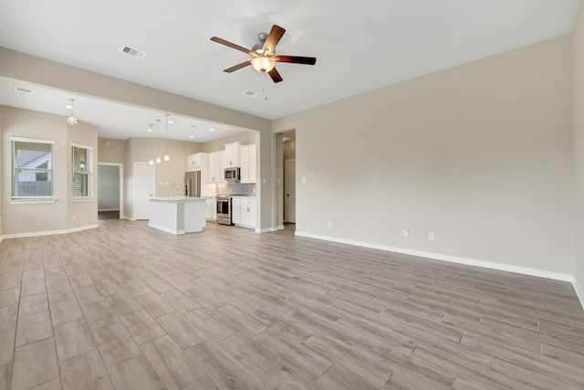 unfurnished living room with ceiling fan, a sink, visible vents, baseboards, and light wood-type flooring