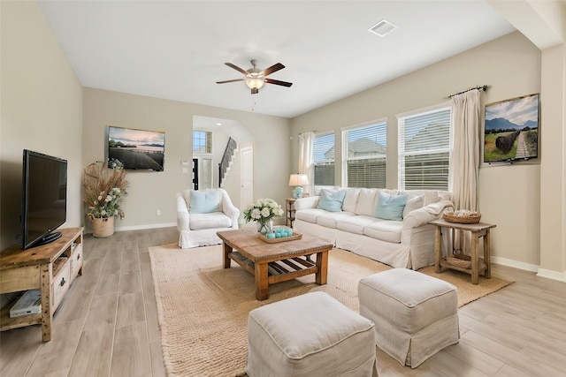 living room featuring light wood-type flooring, visible vents, baseboards, and stairs