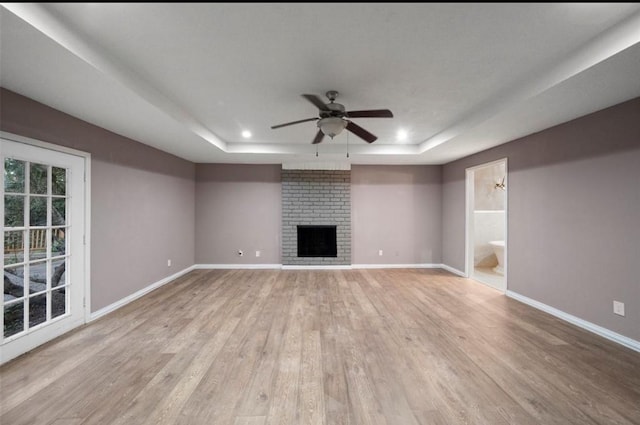 unfurnished living room featuring ceiling fan, a fireplace, a raised ceiling, and light hardwood / wood-style floors