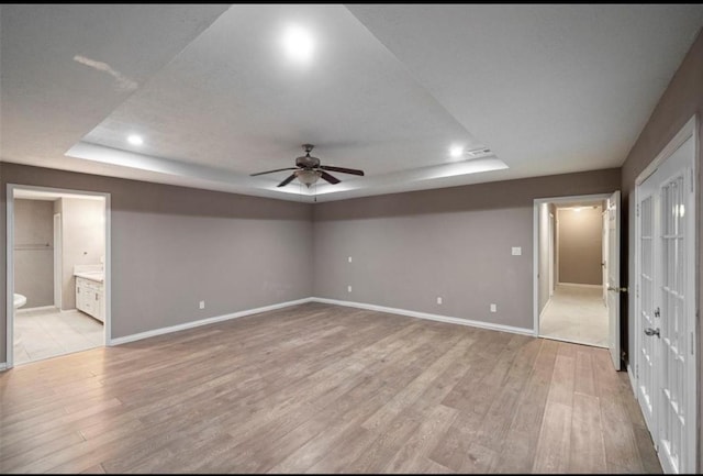 interior space with ceiling fan, ensuite bathroom, a raised ceiling, and light hardwood / wood-style flooring