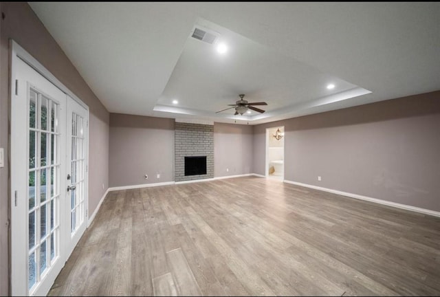 unfurnished living room with ceiling fan, a fireplace, a raised ceiling, and wood-type flooring