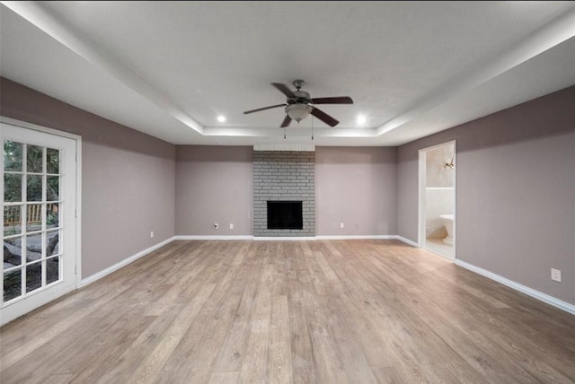 unfurnished living room featuring ceiling fan, a fireplace, light wood-type flooring, and a tray ceiling