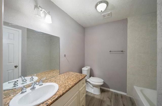 bathroom featuring toilet, a textured ceiling, vanity, hardwood / wood-style flooring, and a washtub