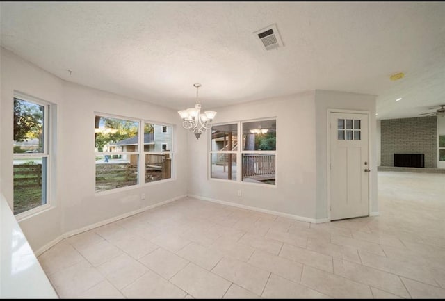 unfurnished room featuring a brick fireplace, ceiling fan with notable chandelier, a textured ceiling, and light tile patterned floors