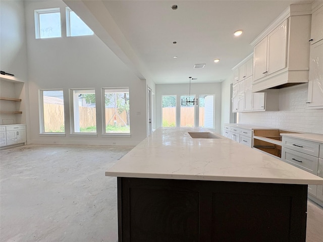 8545 Ridgepoint Dr, Houston, TX 77055 - kitchen featuring white cabinets, a center island with sink, decorative backsplash, light stone counters, and recessed lighting