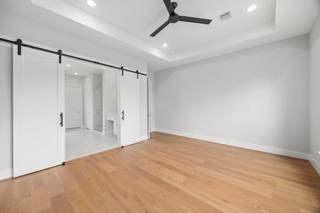 8545 Ridgepoint Dr, Houston, TX 77055 - unfurnished bedroom with a barn door, a raised ceiling, recessed lighting, light wood-type flooring, and ceiling fan