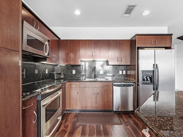 kitchen with sink, dark hardwood / wood-style floors, dark stone counters, and appliances with stainless steel finishes