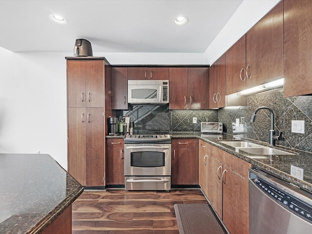 kitchen featuring appliances with stainless steel finishes, sink, dark wood-type flooring, and dark stone counters