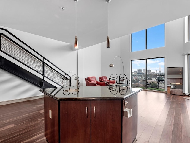 kitchen featuring decorative light fixtures, a center island, dark hardwood / wood-style floors, dark stone counters, and a high ceiling