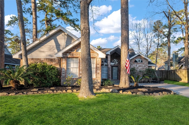 view of front of house featuring brick siding, a front lawn, and fence