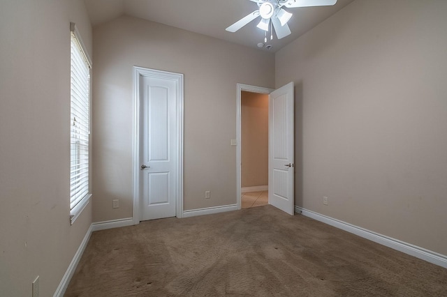 unfurnished bedroom featuring multiple windows, vaulted ceiling, carpet flooring, and ceiling fan