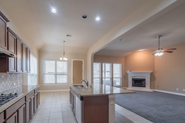 kitchen with sink, appliances with stainless steel finishes, a kitchen island with sink, light stone counters, and vaulted ceiling