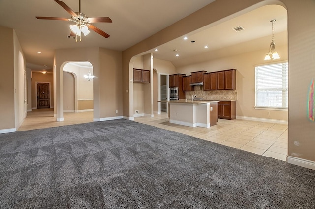 kitchen featuring sink, light colored carpet, an island with sink, ceiling fan, and decorative backsplash