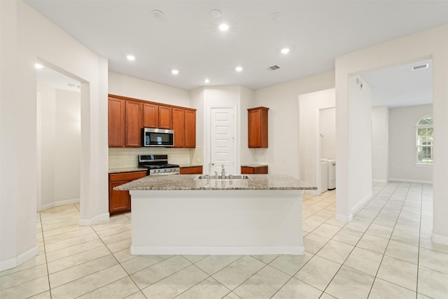 kitchen with sink, appliances with stainless steel finishes, a kitchen island with sink, light stone countertops, and decorative backsplash