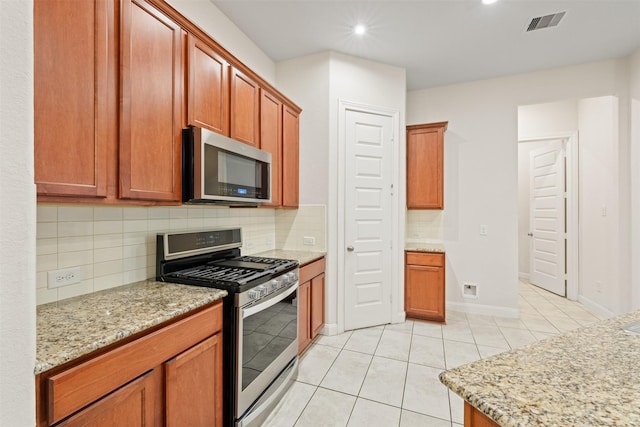 kitchen featuring light stone countertops, appliances with stainless steel finishes, light tile patterned floors, and decorative backsplash