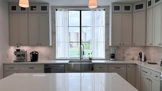 kitchen featuring tasteful backsplash, dishwasher, sink, hanging light fixtures, and light stone countertops