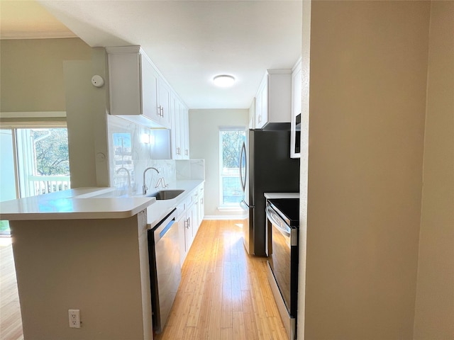 kitchen with stainless steel appliances, a peninsula, a sink, white cabinets, and light countertops