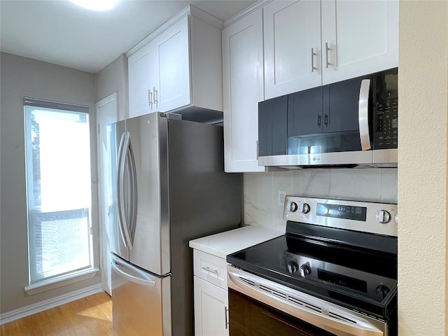 kitchen featuring light countertops, backsplash, appliances with stainless steel finishes, light wood-style floors, and white cabinets