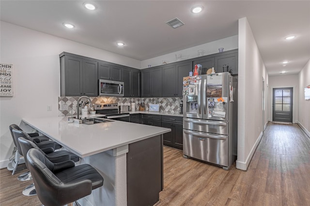 kitchen featuring a breakfast bar area, stainless steel appliances, light countertops, a sink, and a peninsula