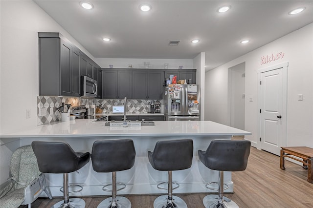 kitchen with a breakfast bar area, a peninsula, stainless steel appliances, a sink, and light countertops