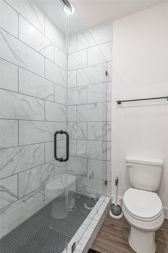 bathroom with toilet, a stall shower, baseboards, and wood finished floors