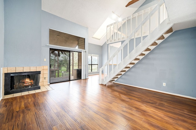 unfurnished living room with a textured ceiling, high vaulted ceiling, a fireplace, wood finished floors, and baseboards