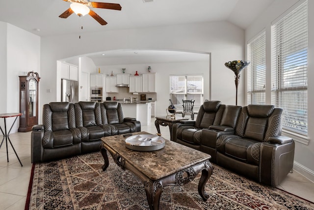 living area with light tile patterned floors, ceiling fan, arched walkways, and lofted ceiling