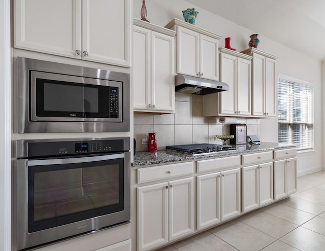 9518 Brannok Ln, Tomball, TX 77375 - kitchen with appliances with stainless steel finishes, under cabinet range hood, stone countertops, light tile patterned floors, and tasteful backsplash