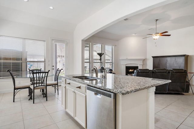 kitchen featuring stainless steel dishwasher, light tile patterned flooring, a sink, light stone countertops, and a lit fireplace