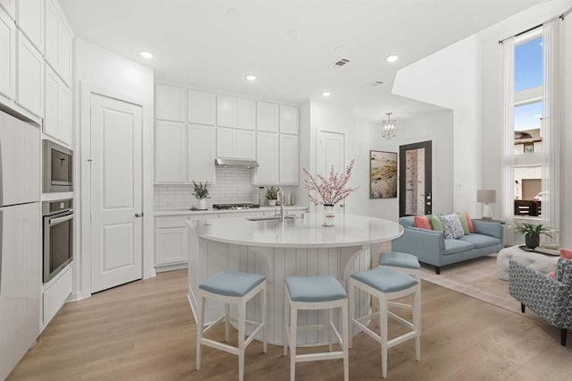 kitchen with sink, appliances with stainless steel finishes, white cabinetry, a center island with sink, and light wood-type flooring