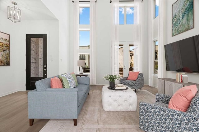 living room with a high ceiling, a chandelier, light wood-type flooring, and french doors