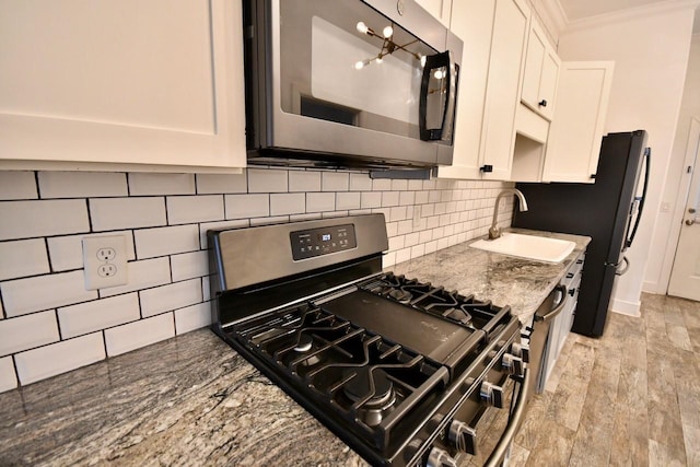 kitchen featuring a sink, white cabinetry, light wood-style floors, appliances with stainless steel finishes, and decorative backsplash