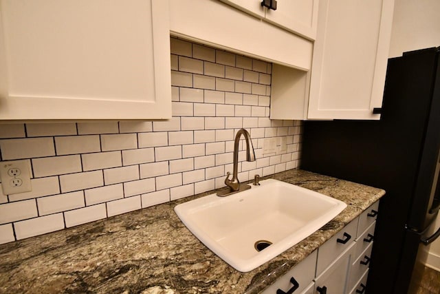 kitchen featuring dark stone counters, tasteful backsplash, a sink, and white cabinetry